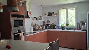 Ett modernt kök med en central köksö, ett matbord med stolar och ett stort fönster som släpper in naturligt ljus.