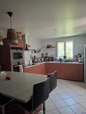 Eine moderne Küche mit einer zentralen Kochinsel, einem Esstisch mit Stühlen und einem großen Fenster für natürliches Licht.