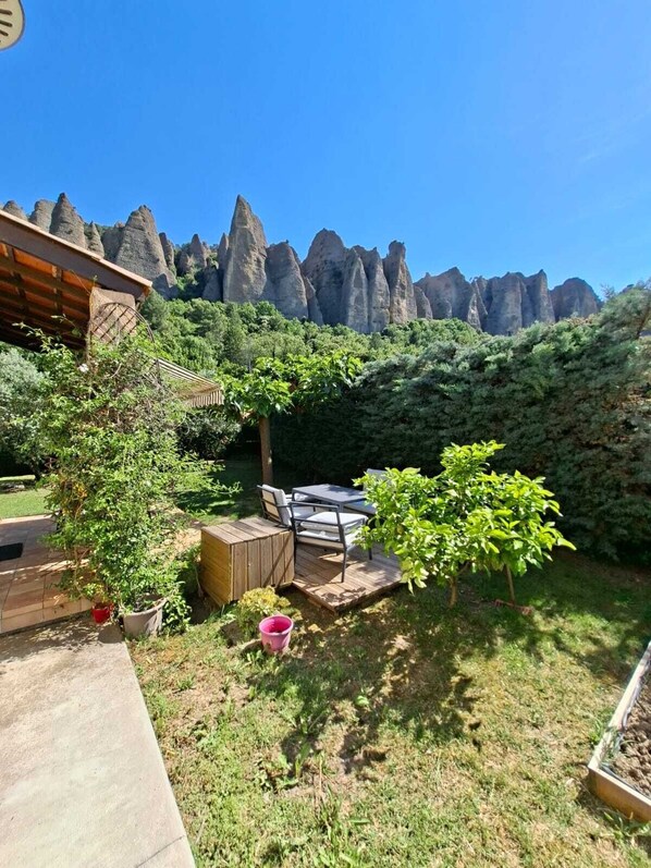 Eine Terrasse mit Tisch und Stühlen, umgeben von Grünpflanzen und Blick auf Felsformationen.