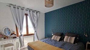 Ett sovrum med en säng, ett skrivbord, en spegel och ett fönster med gardiner.