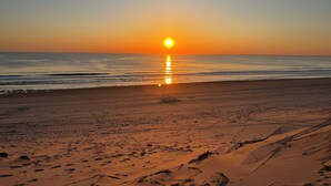 Una spiaggia con impronte che conducono all'acqua, un cielo sereno e il sole che tramonta o sorge.