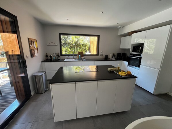 Een moderne keuken met een centraal kookeiland, witte kastjes, een raam met uitzicht en geïntegreerde apparatuur.