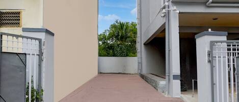 A narrow alleyway between two buildings with gated entrances, a concrete pathway, and a small garden area with trees.