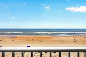 Ein Strand mit blauem Himmel, sandigem Ufer und einem Geländer im Vordergrund.