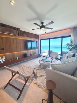 Ein modernes Wohnzimmer mit großem Fernseher, Deckenventilator, Sofa und Meerblick.