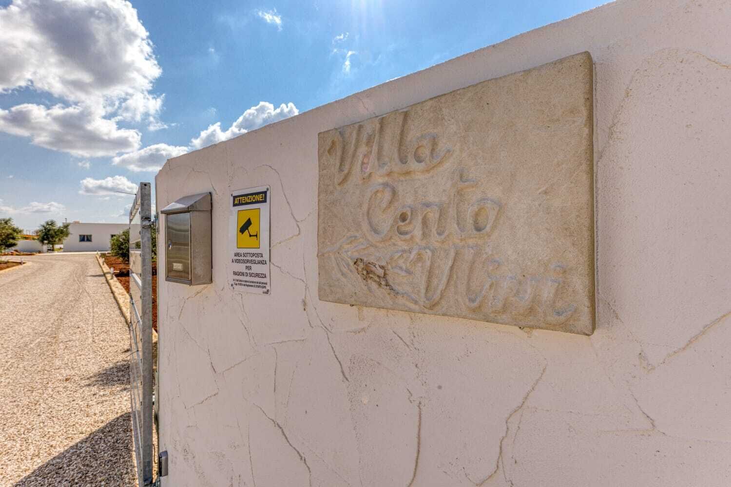 Un mur sur lequel est gravé le nom « Villa Centro Vigni », une caméra de surveillance et un panneau d’avertissement.