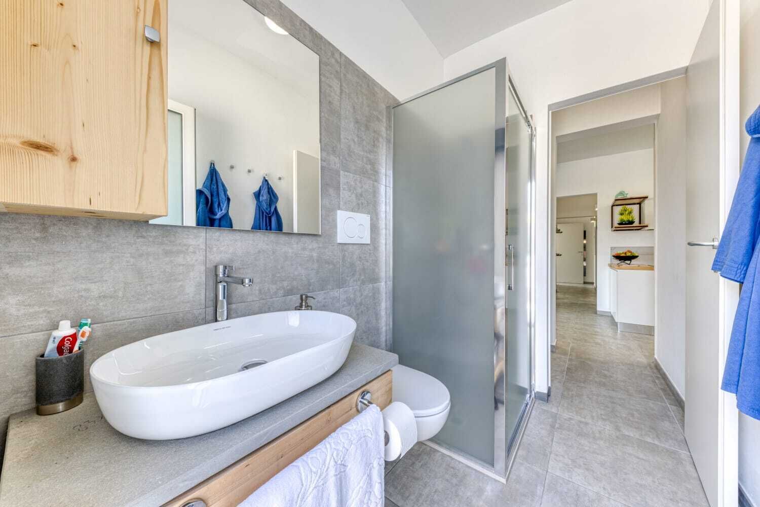 Ein modernes Badezimmer mit einem großen, weißen Waschbecken, einer Duschkabine aus Glas und einem Holzkabinet.