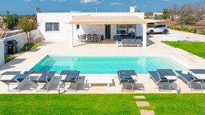 Ein modernes Haus mit Swimmingpool, Sitzgelegenheiten im Freien und einem geparkten Auto in der Nähe.