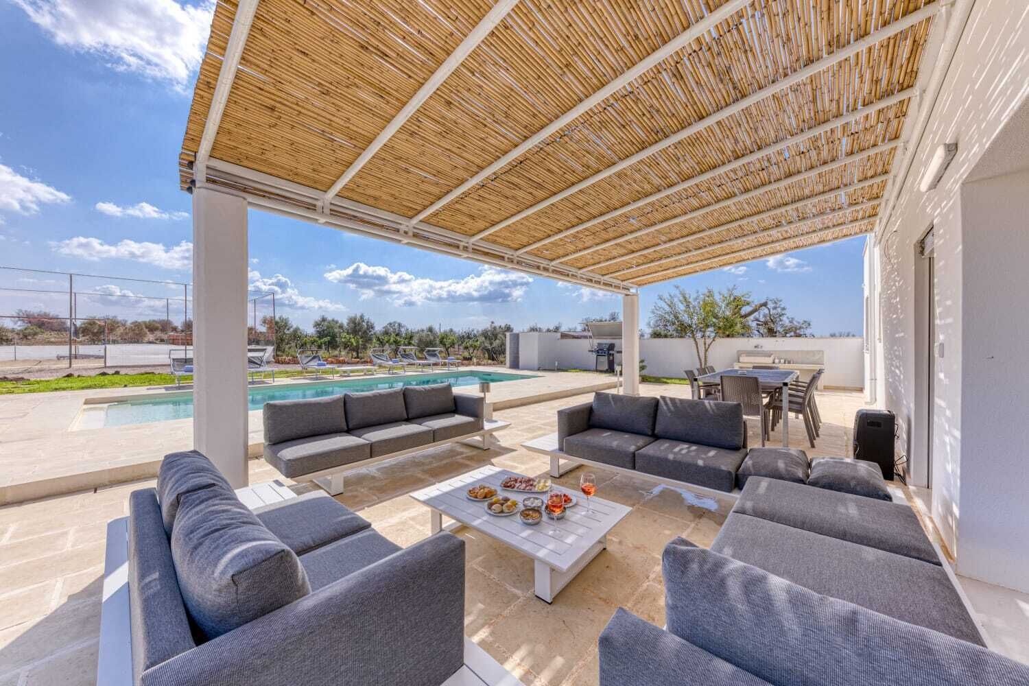 Ein überdachter Außenbereich mit Pool, Sofas und einem Tisch mit Speisen und Getränken.