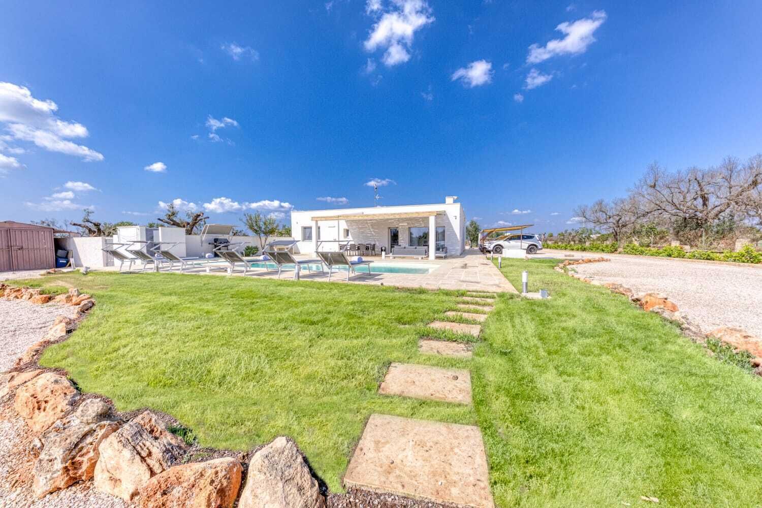 A modern house with a swimming pool, outdoor seating, and a well-maintained lawn.