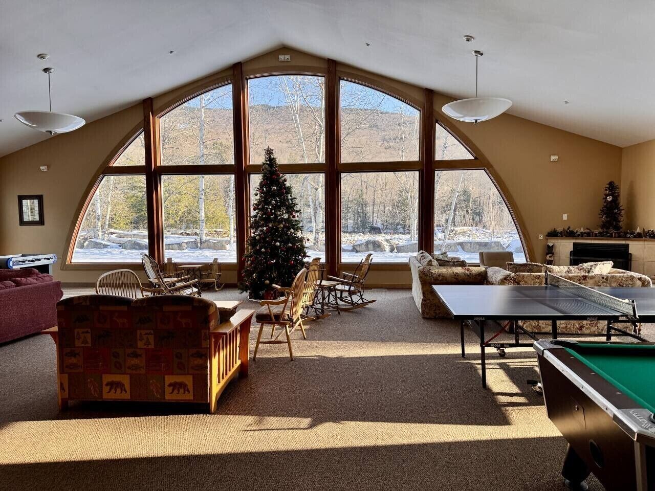 Une pièce spacieuse avec une grande fenêtre en arc de cercle, une table de ping-pong et un sapin de Noël.