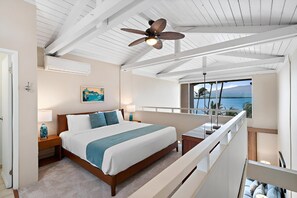 Ein Schlafzimmer mit einem Bett, einem Nachttisch, einer Lampe, einem Deckenventilator und Blick auf den Ozean.