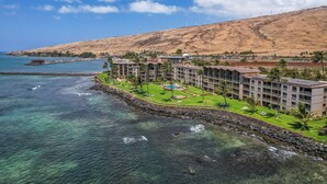 A coastal hotel with a pool, beachfront view, and wind turbines in the background. - Oceanview 2BR/2BA Condo w/ Pool, A/C, Balcony & Beach Access – Maalaea Kai 403 (Wailuku)