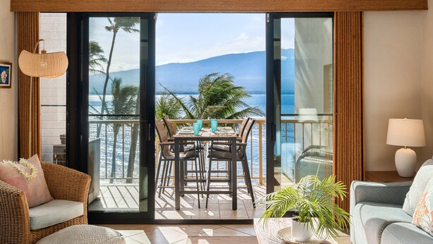 A balcony with a table and chairs, a wicker sofa, a potted plant, and a view of the ocean and mountains. - Oceanview 2BR/2BA Condo w/ Pool, A/C, Balcony & Beach Access – Maalaea Kai 403 (Wailuku)
