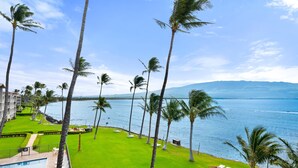 A resort with a pool, green lawn, palm trees, and a view of the ocean. - Oceanview 2BR/2BA Condo w/ Pool, A/C, Balcony & Beach Access – Maalaea Kai 403 (Wailuku)