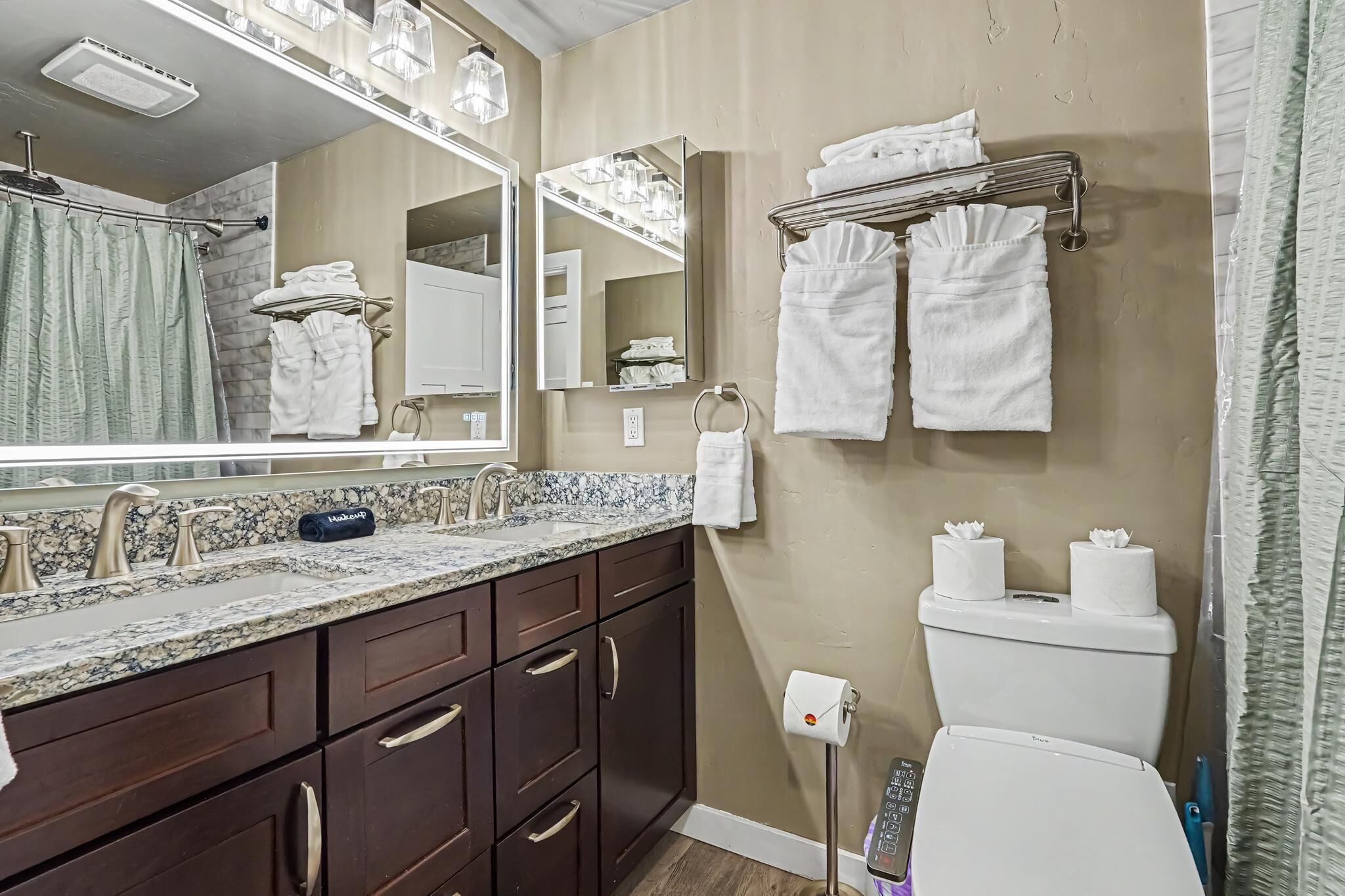 A bathroom with a marble sink, dark wooden cabinets, a large mirror, and a toilet with toilet paper.
