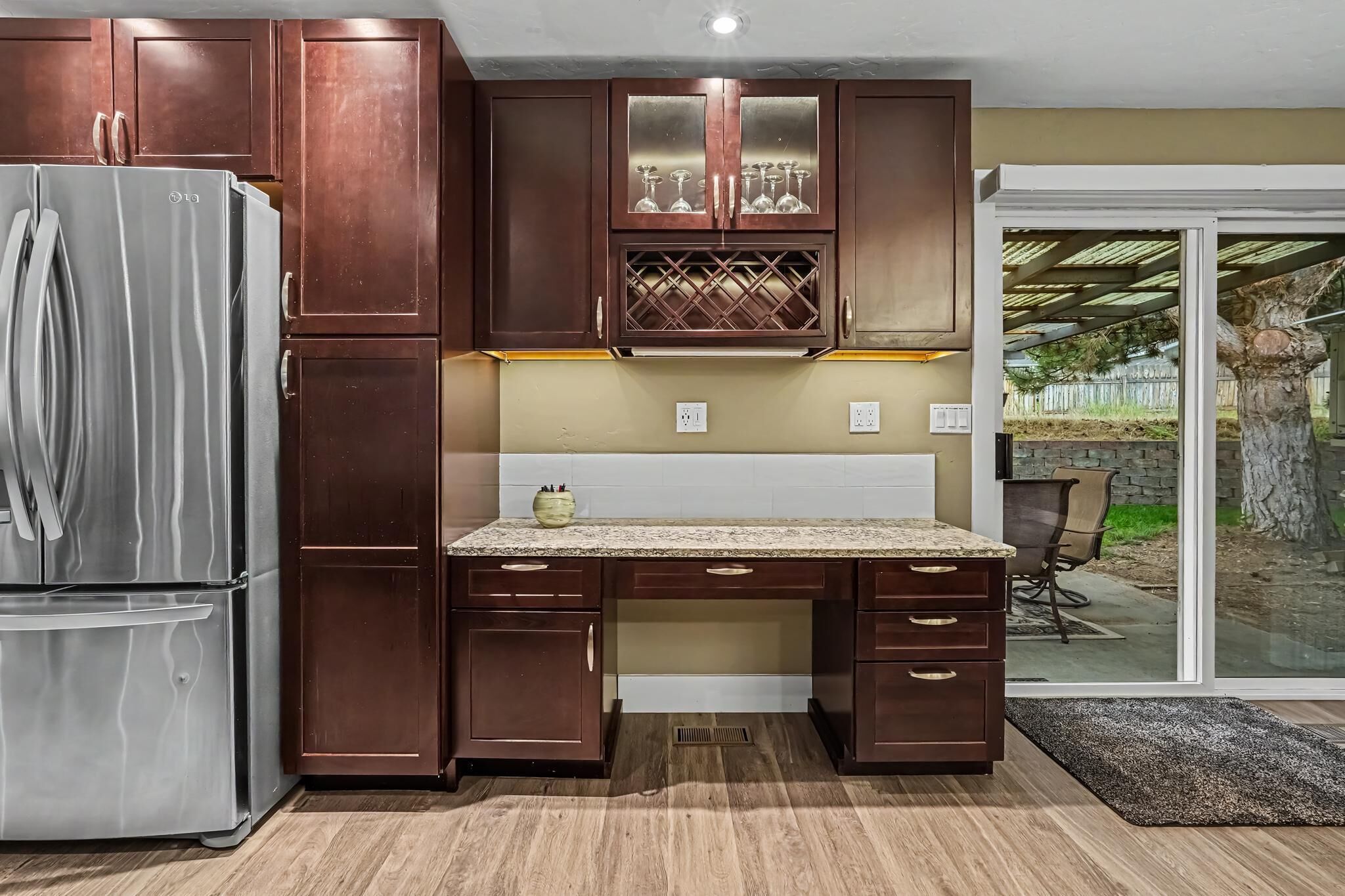 A kitchen with dark wooden cabinets, a stainless steel refrigerator, and a granite countertop.