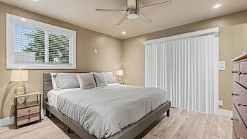 Une chambre à coucher comprenant un lit, une table de chevet, un ventilateur de plafond, une fenêtre avec des stores et un interrupteur fixé au mur.