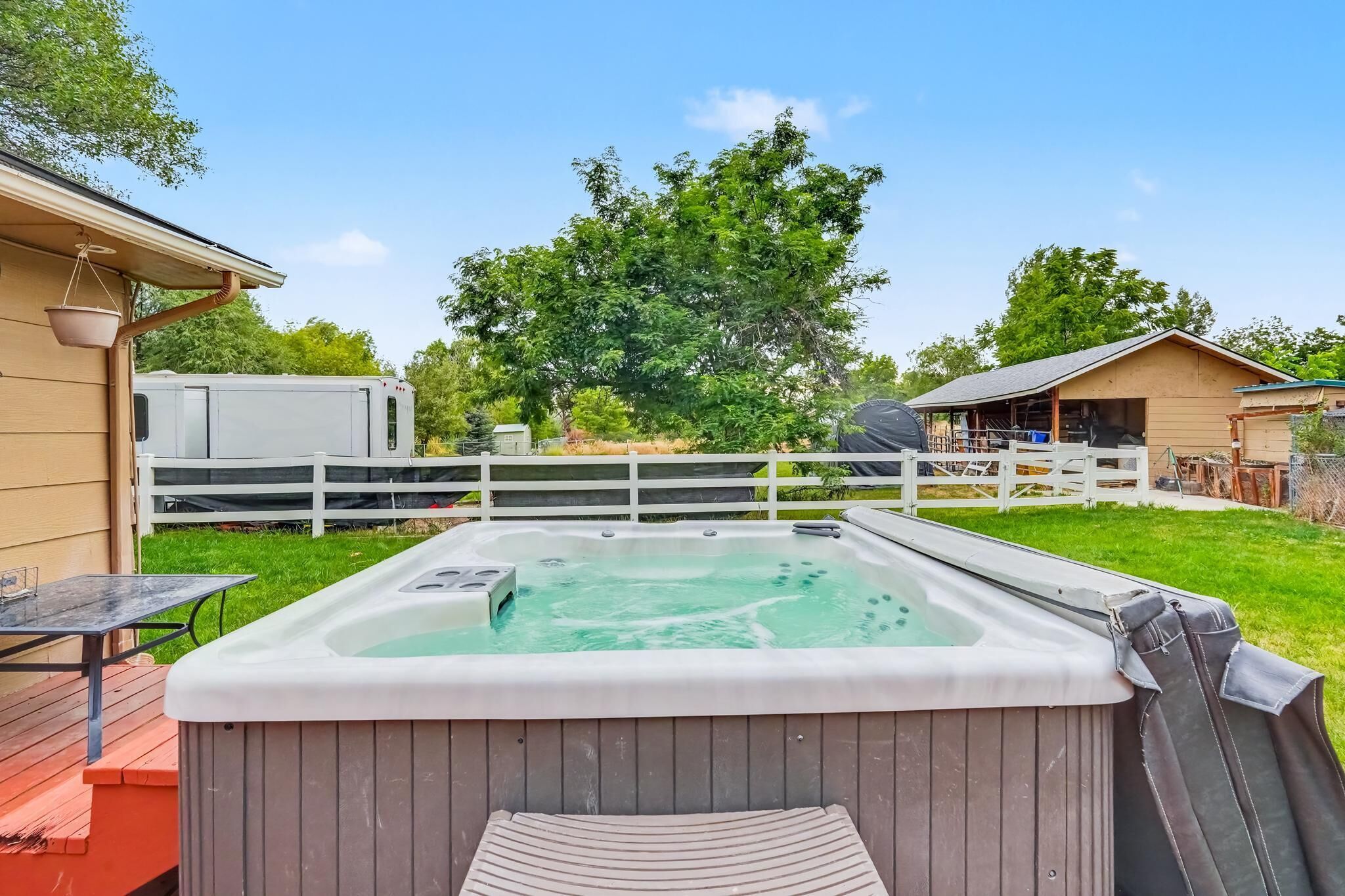 A hot tub on a wooden deck with a white fence and trees in the background.
