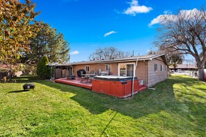 A single-story house with a covered patio, a hot tub, and a lawn.
