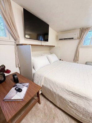 Habitación de hotel con cama, escritorio con control remoto, televisor de pantalla plana y equipo de aire acondicionado.
