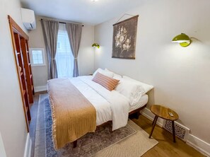 A bedroom with a bed, a small round table, a wall-mounted lamp, and a window with curtains.