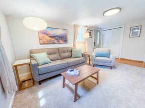 Una sala de estar con sofá, sillón, mesa de centro y un cuadro en la pared.