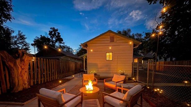 Une terrasse en bois, dotée de mobilier d’extérieur et d’un foyer, entourée d’une clôture en bois et d’un arbre.