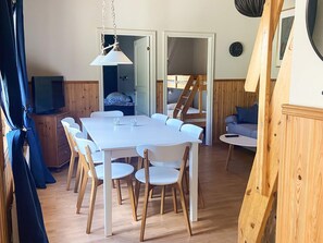 A room with a white table, chairs, a TV, bunk beds, and a wooden floor.