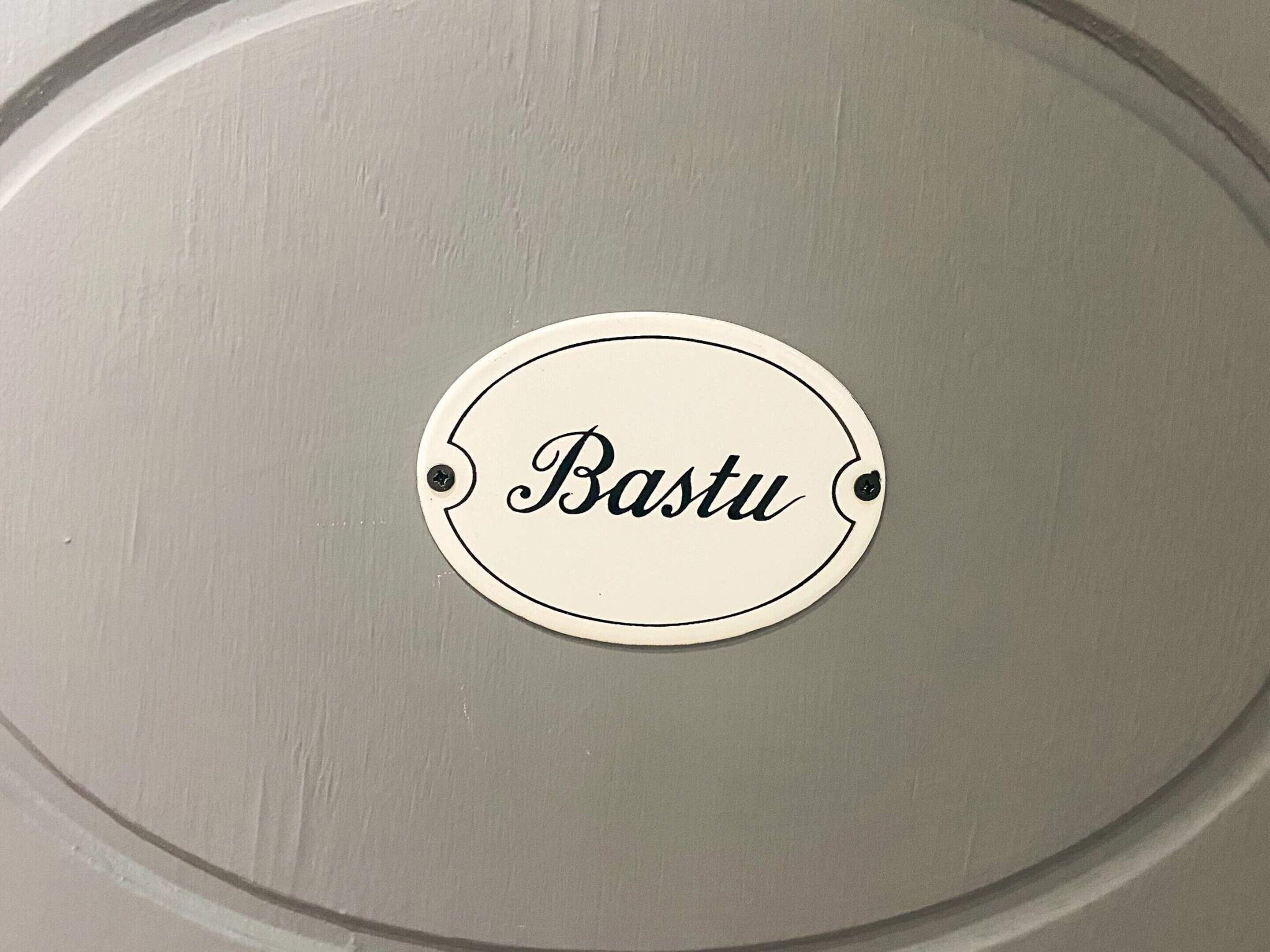 Un letrero circular con la palabra 'Bastu' escrita, fijado a una pared.