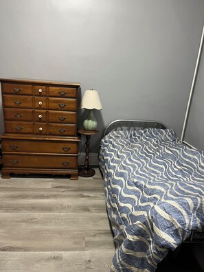 Ein Schlafzimmer mit einem hölzernen Schminktisch, einer Lampe und einem Bett mit gemustertem Überwurf.