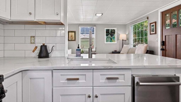 Una cocina moderna con armarios blancos, un refrigerador de acero inoxidable y una encimera de mármol.