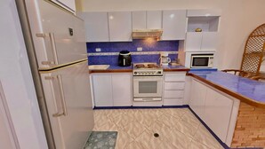 Cocina compacta con armarios blancos, estufa integrada, microondas y cafetera.