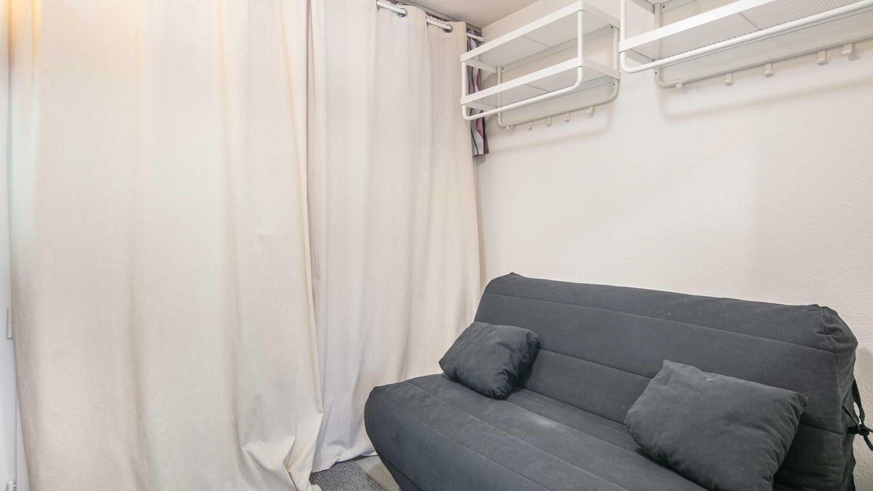 Una habitación con un sofá gris, cortinas blancas y una pared blanca.