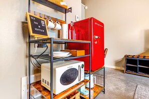 A kitchenette with a red refrigerator, a white microwave, and a shelf with dishes and a sign. - Cozy studio with AC walk to FIFA (Seattle)