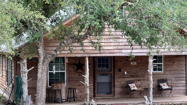 A rustic wooden building with a porch, a door, and a window. - RiverBend Retreat 
Cozy 1 bedroom, 2 loft cabin. (Leakey)
