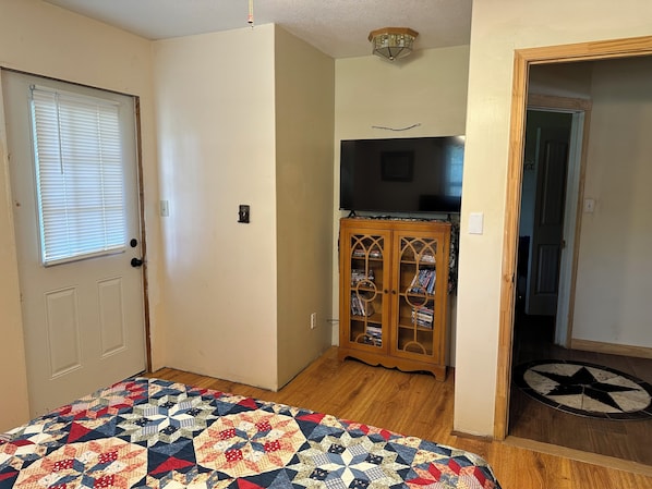 Une pièce avec une porte en bois, un mur blanc, un luminaire au plafond, un meuble en bois doté de portes en verre et un tapis au motif décoratif.