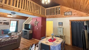 A wooden interior with a staircase, a dining area, and a television. - RiverBend Retreat 
Cozy 1 bedroom, 2 loft cabin. (Leakey)