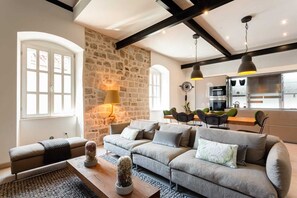 Ein modernes Wohnzimmer mit Steinwand, einer Sofagarnitur, einem Essbereich und einer Küche im Hintergrund.