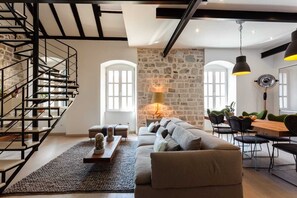 Ein modernes Wohnzimmer mit Steinwand, Treppe, einer Couch, einem Esstisch und Pendelleuchten.
