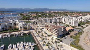 A marina with boats, a hotel with multiple floors, and a coastal view. - BRIGHT STUDIO WITH TERRACE FACING THE SEA AND MARINA (Le Barcarès)