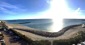 A coastal view with a parking area, a beach, and a rocky breakwater. - BRIGHT STUDIO WITH TERRACE FACING THE SEA AND MARINA (Le Barcarès)