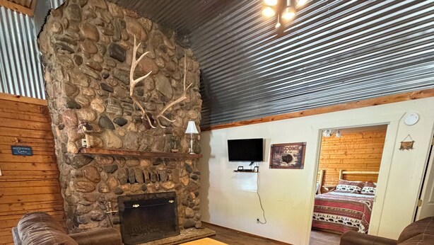 A cozy living room with a stone fireplace, leather sofas, a wooden coffee table, and a ceiling fan.