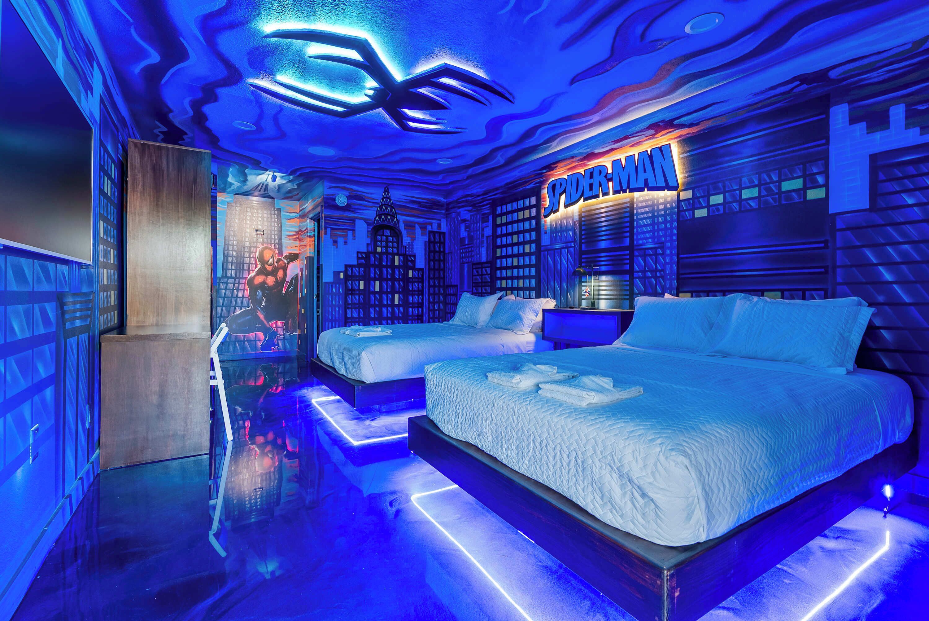 A room with two beds, a cityscape mural, and a neon sign reading 'SPIDER-MAN'.