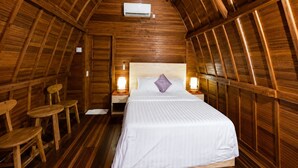 Un dormitorio acogedor en el ático con techo de madera, una cama con ropa de cama blanca, dos mesitas de noche con lámparas y una pequeña silla de madera.