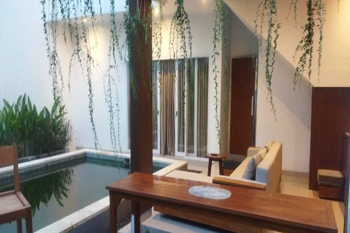 Ein moderner Außenbereich mit Sitzgelegenheit, Pool, Holzmöbeln und hängenden Pflanzen.