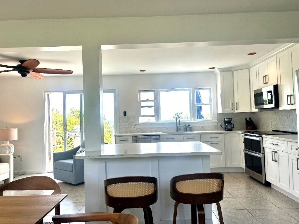 Een moderne keuken met witte kasten, een groot eiland en een eethoek met twee stoelen.