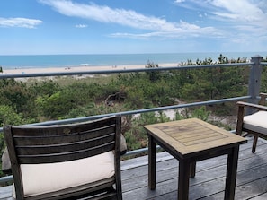 A wooden deck with a table and chairs overlooking a beach.