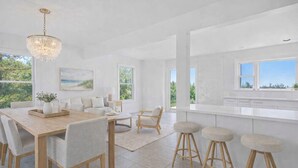 A modern kitchen with white cabinets, a wooden dining table, and bar stools. - Oceanfront Retreat • Modern Coastal • New (Cherry Grove)