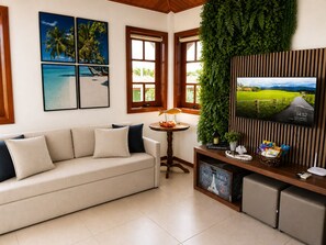 Een woonkamer met een bank, een televisie, een kleine tafel met een lamp en een decoratieve plant.